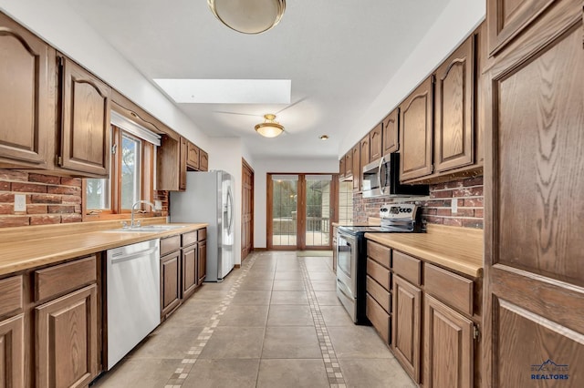 kitchen featuring sink, light tile patterned floors, appliances with stainless steel finishes, tasteful backsplash, and french doors