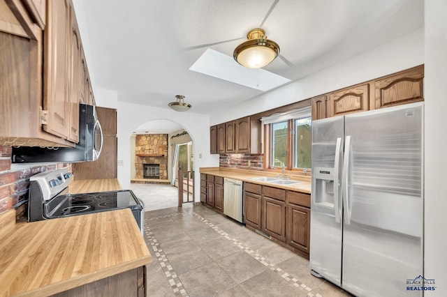 kitchen featuring a stone fireplace, sink, light tile patterned floors, appliances with stainless steel finishes, and backsplash