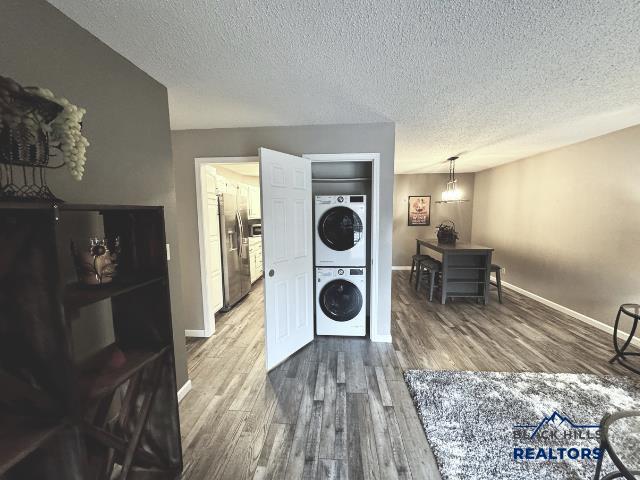 laundry room featuring stacked washer / dryer, wood-type flooring, and a textured ceiling