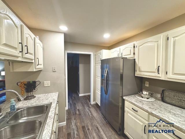 kitchen with dark wood-type flooring, sink, light stone counters, stainless steel fridge, and white cabinets