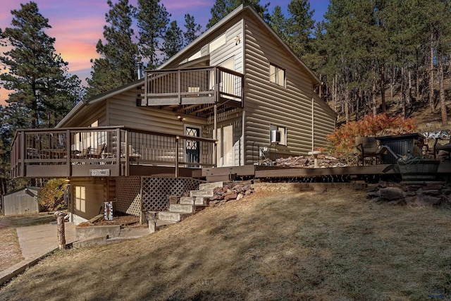 back house at dusk featuring a wooden deck and a yard