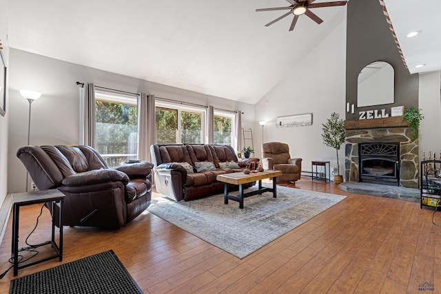 living room featuring ceiling fan, a stone fireplace, light wood-type flooring, and high vaulted ceiling