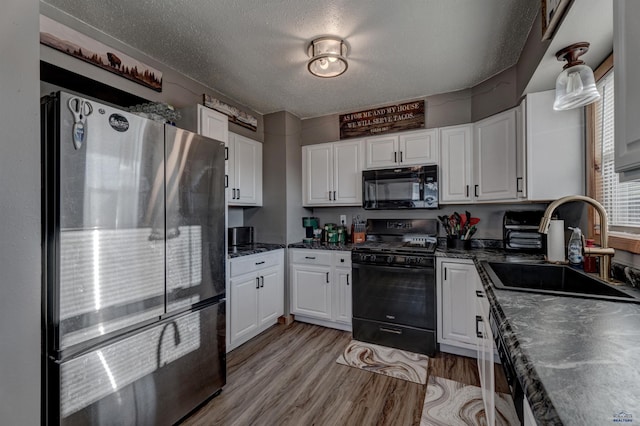 kitchen featuring sink, white cabinetry, light hardwood / wood-style flooring, a textured ceiling, and black appliances