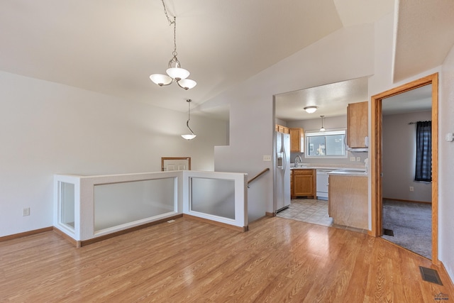 kitchen with white appliances, decorative light fixtures, vaulted ceiling, and light wood-type flooring