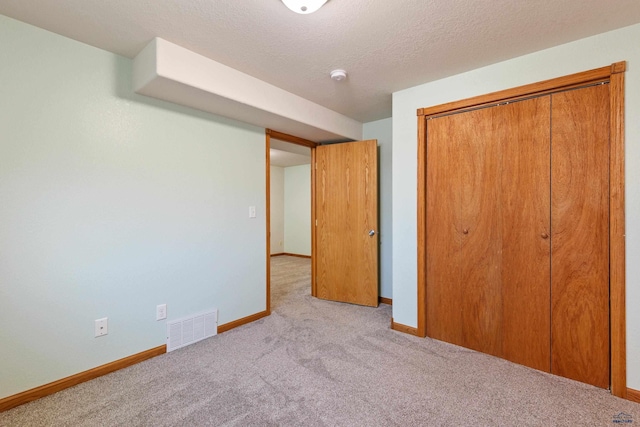 unfurnished bedroom with light colored carpet, a closet, and a textured ceiling