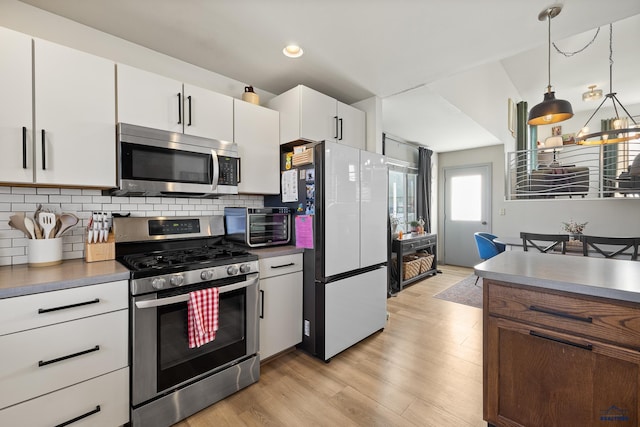 kitchen featuring light wood-type flooring, pendant lighting, stainless steel appliances, decorative backsplash, and white cabinets