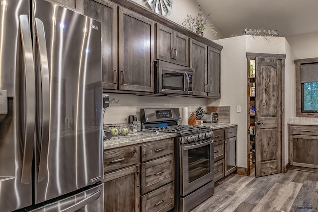 23232 Clear Creek Rd, Rapid City, SD 57702 - kitchen with lofted ceiling, stainless steel appliances, dark brown cabinetry, light stone countertops, and light hardwood / wood-style floors