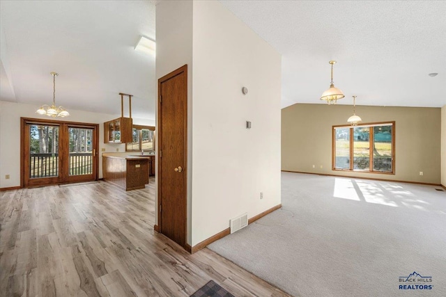 unfurnished living room featuring lofted ceiling, a notable chandelier, a wealth of natural light, and light wood-type flooring