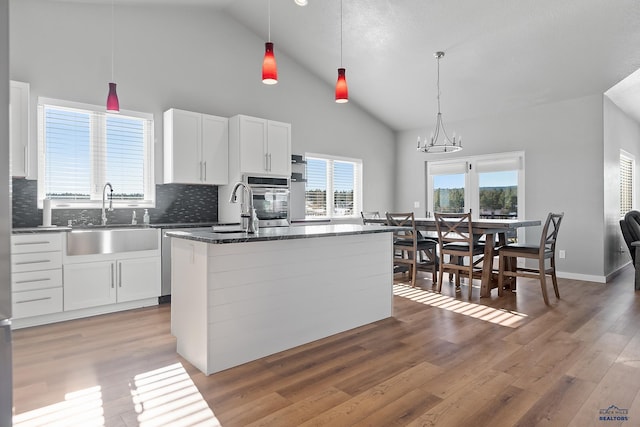 kitchen with sink, white cabinets, a kitchen island, decorative light fixtures, and oven