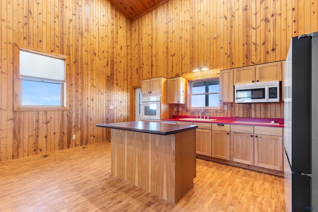 kitchen with sink, black fridge, wooden walls, a kitchen island, and oven