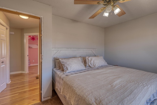 bedroom with ceiling fan, light wood-type flooring, and a textured ceiling