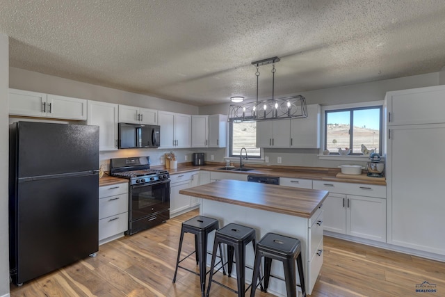 kitchen featuring white cabinetry, wooden counters, a kitchen island, and black appliances