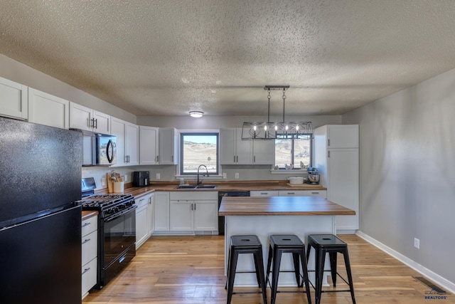 kitchen featuring a kitchen island, pendant lighting, butcher block countertops, white cabinetry, and black appliances