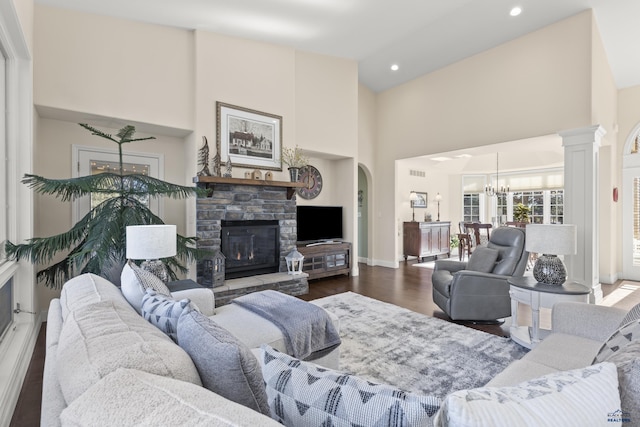 living room with a stone fireplace, ornate columns, high vaulted ceiling, dark hardwood / wood-style floors, and a notable chandelier