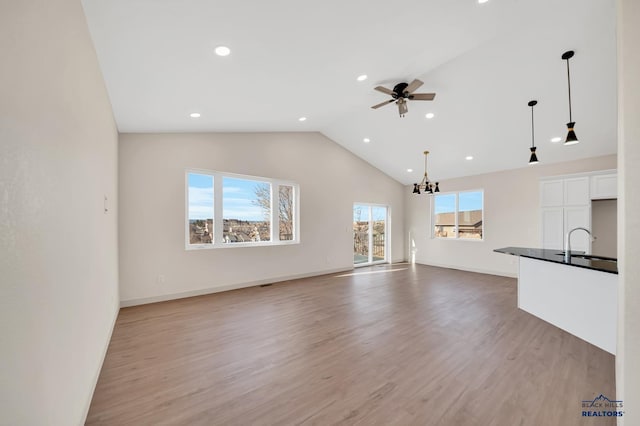 unfurnished living room with sink, ceiling fan with notable chandelier, vaulted ceiling, and light wood-type flooring