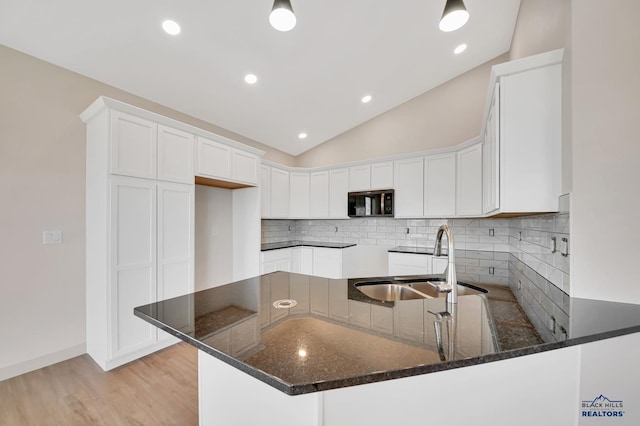 kitchen with sink, kitchen peninsula, white cabinets, vaulted ceiling, and dark stone counters