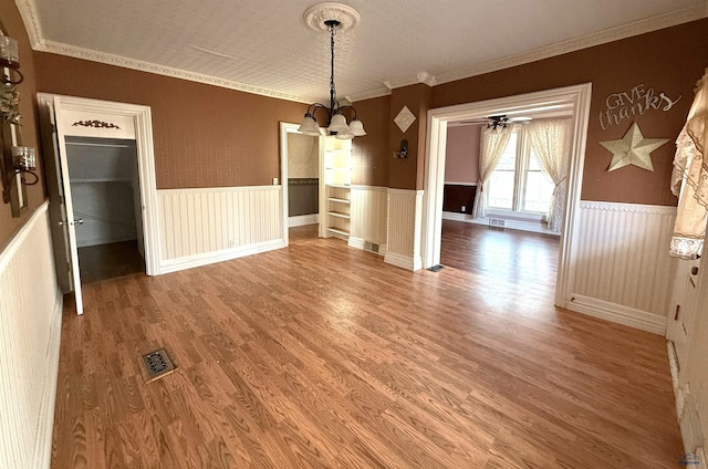 unfurnished dining area with crown molding, wood-type flooring, and a chandelier