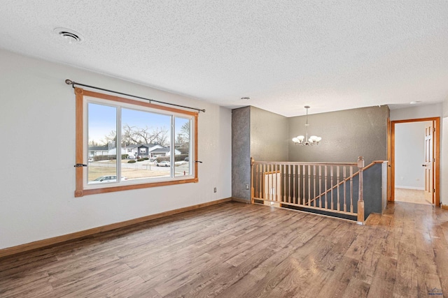 unfurnished room featuring hardwood / wood-style flooring, a textured ceiling, and a notable chandelier