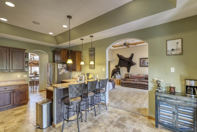 kitchen with dark brown cabinetry, a breakfast bar area, decorative light fixtures, stainless steel fridge, and light stone countertops