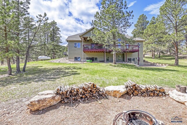 rear view of property with a wooden deck, a fire pit, and a lawn