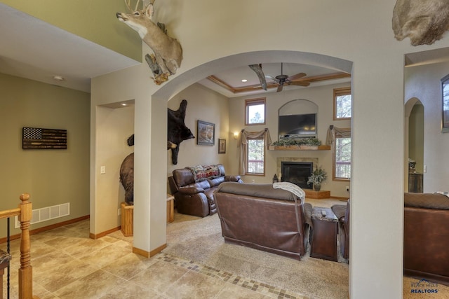 living room featuring a tray ceiling, light tile patterned floors, crown molding, and ceiling fan