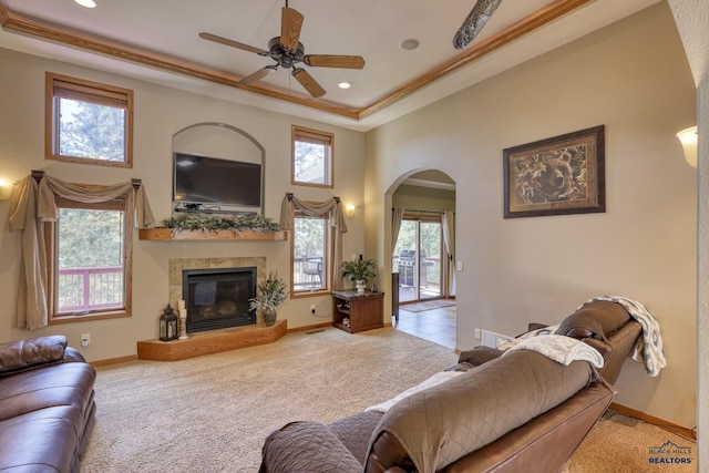 carpeted living room featuring crown molding, ceiling fan, a towering ceiling, a tiled fireplace, and a raised ceiling