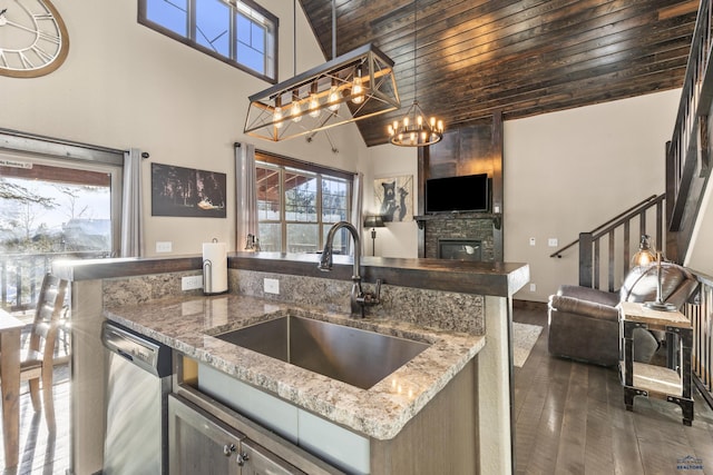 kitchen with a stone fireplace, decorative light fixtures, dishwasher, sink, and light stone countertops