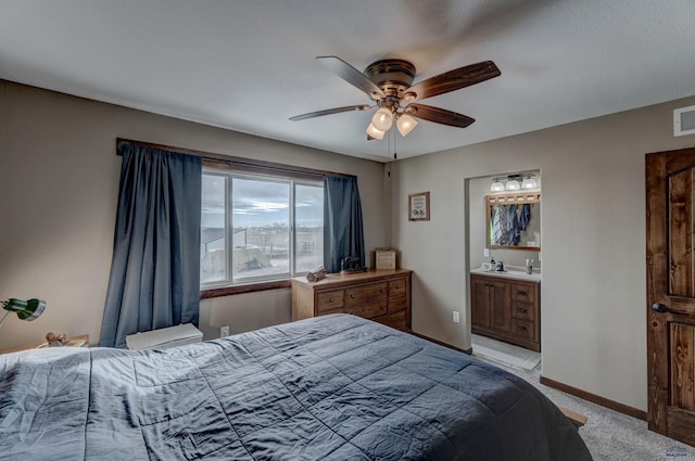 bedroom with ceiling fan, light colored carpet, and ensuite bath