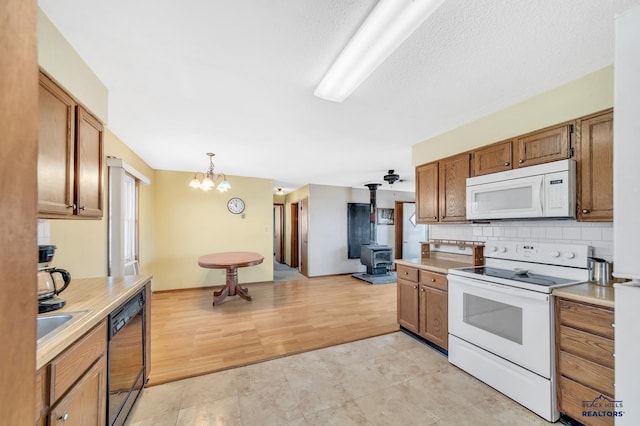 kitchen with pendant lighting, white appliances, a notable chandelier, decorative backsplash, and a wood stove