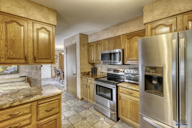 kitchen with light stone counters, a textured ceiling, and appliances with stainless steel finishes