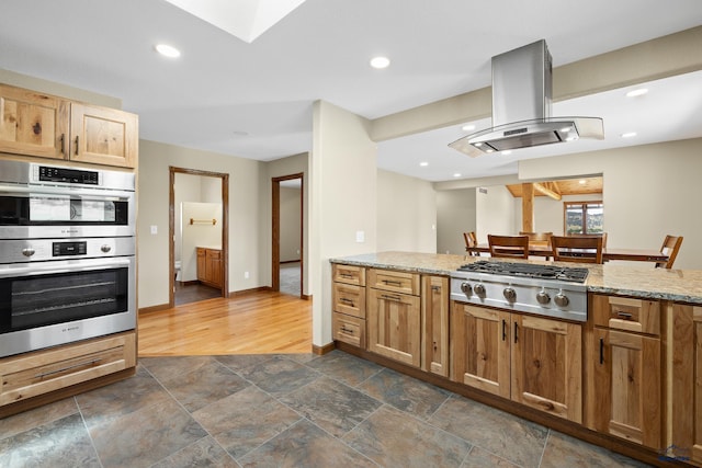 kitchen with island exhaust hood, appliances with stainless steel finishes, dark hardwood / wood-style flooring, and light stone countertops