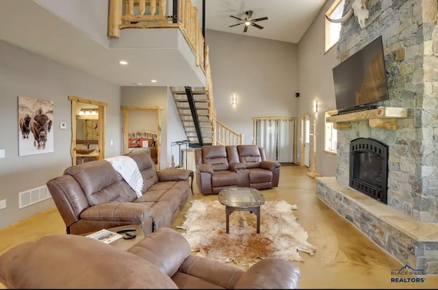 living room with a stone fireplace, ceiling fan, and a high ceiling