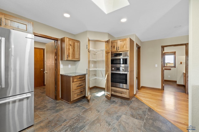 kitchen with appliances with stainless steel finishes, dark hardwood / wood-style flooring, a skylight, and light stone countertops