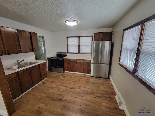 kitchen featuring sink, stainless steel appliances, dark brown cabinetry, a textured ceiling, and light wood-type flooring