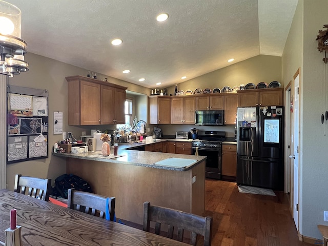 kitchen with dark wood-type flooring, lofted ceiling, range with gas stovetop, refrigerator with ice dispenser, and kitchen peninsula