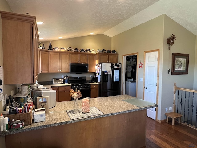 kitchen featuring dark wood-type flooring, kitchen peninsula, vaulted ceiling, and black appliances