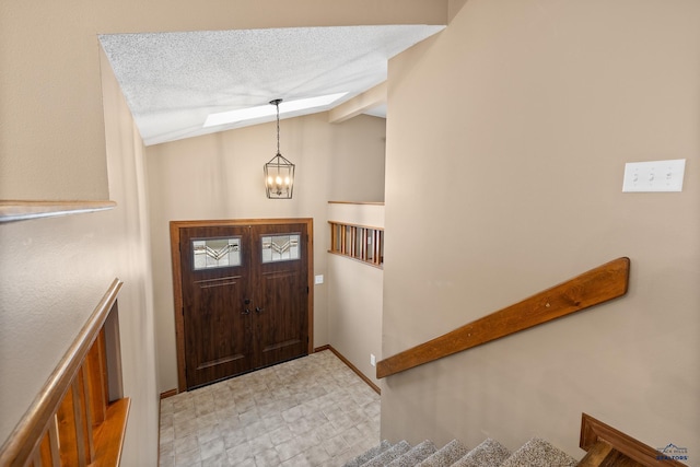 entrance foyer featuring an inviting chandelier, lofted ceiling with skylight, and a textured ceiling