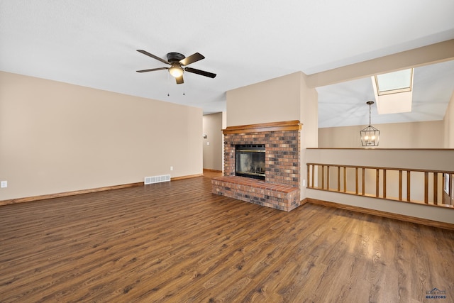 unfurnished living room featuring dark wood-type flooring, ceiling fan with notable chandelier, and a brick fireplace