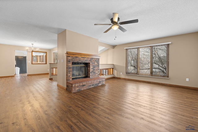 unfurnished living room featuring wood-type flooring, ceiling fan with notable chandelier, a brick fireplace, and a textured ceiling