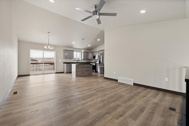 unfurnished living room with dark wood-type flooring, lofted ceiling, sink, and ceiling fan with notable chandelier