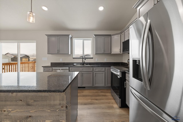 kitchen featuring sink, decorative light fixtures, dark stone counters, dark hardwood / wood-style flooring, and stainless steel appliances