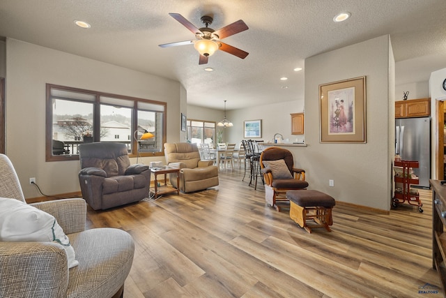 living room featuring ceiling fan with notable chandelier, a textured ceiling, and light wood-type flooring