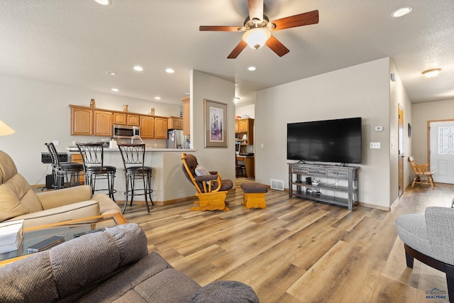 living room featuring ceiling fan, a textured ceiling, and light hardwood / wood-style floors