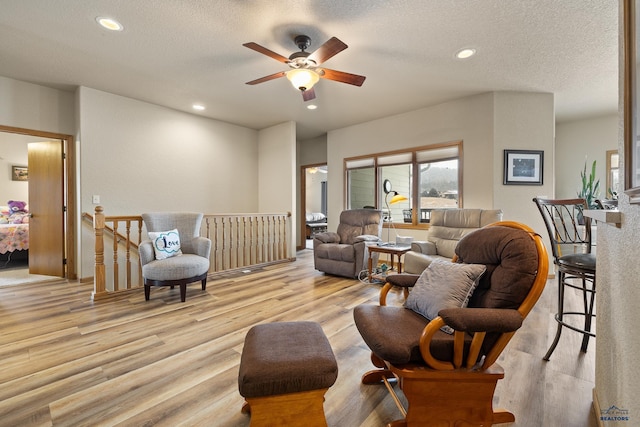 living room featuring ceiling fan, a textured ceiling, and light wood-type flooring