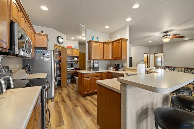 kitchen featuring sink, a breakfast bar area, appliances with stainless steel finishes, kitchen peninsula, and light hardwood / wood-style floors