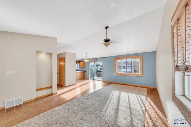 unfurnished living room featuring lofted ceiling, ceiling fan with notable chandelier, a textured ceiling, and light hardwood / wood-style floors