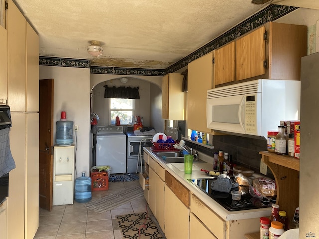 kitchen featuring sink, light tile patterned floors, a textured ceiling, washing machine and clothes dryer, and black electric cooktop