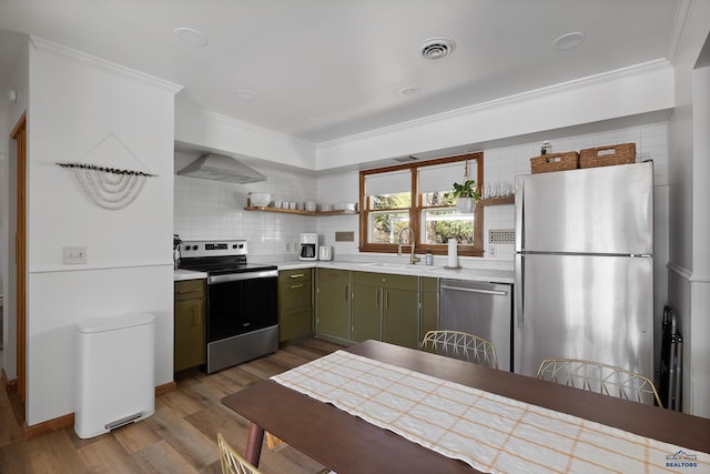 kitchen with sink, stainless steel appliances, ornamental molding, green cabinetry, and wall chimney exhaust hood