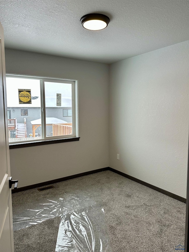 spare room featuring baseboards, visible vents, a textured ceiling, and carpet flooring