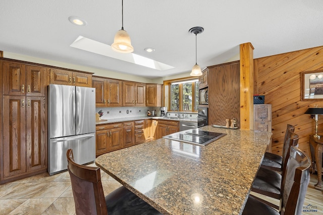 kitchen with a skylight, black appliances, a breakfast bar area, and dark stone counters